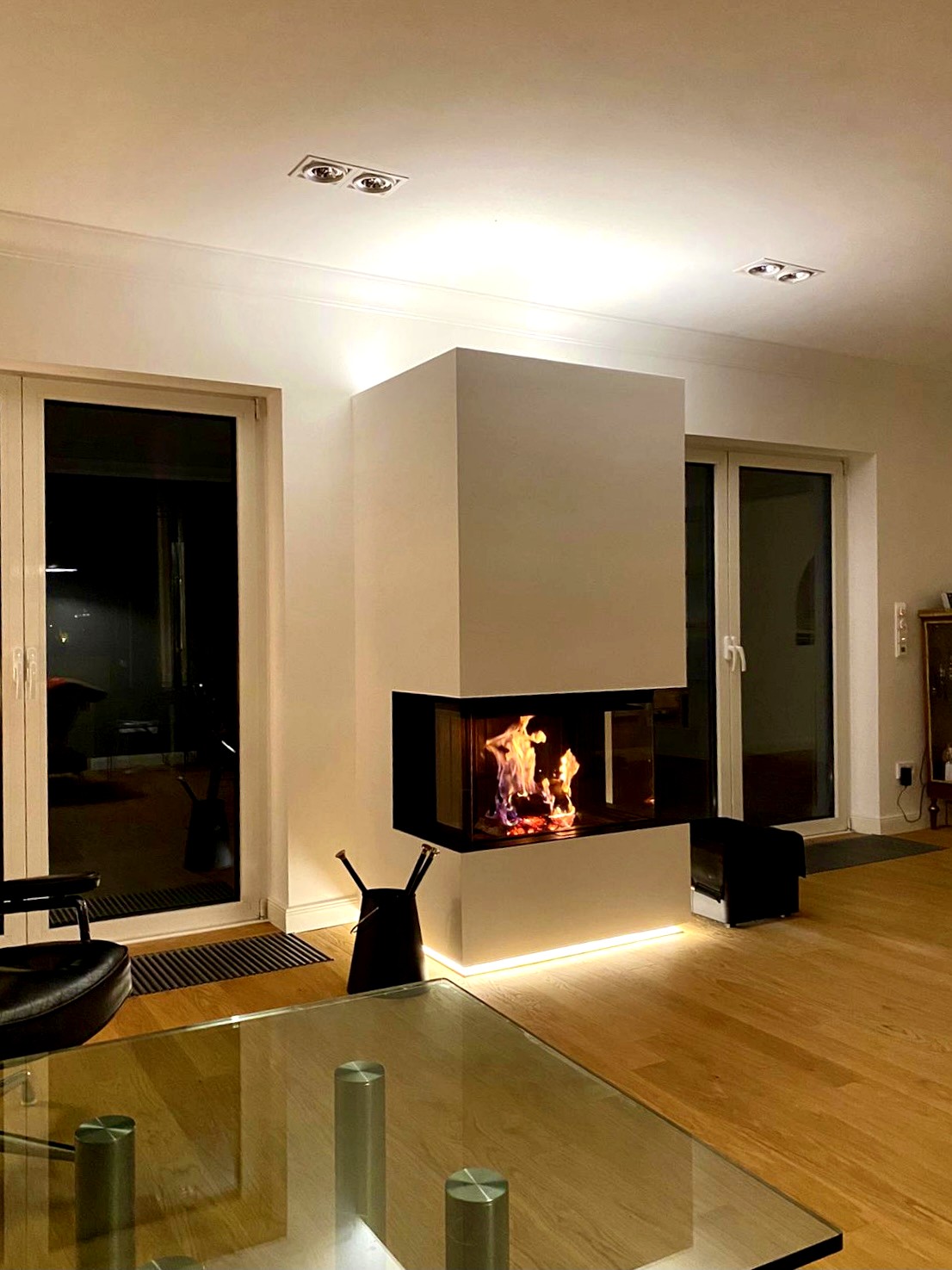 Dreiseitig verglaster Panoramakamin mit moderner LED-Beleuchtung in einem stilvollen Wohnzimmer bei Nacht